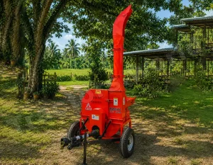 Red towable wood chipper outdoors on a grassy area near trees, with a tall red chute ready to process branches into chips.